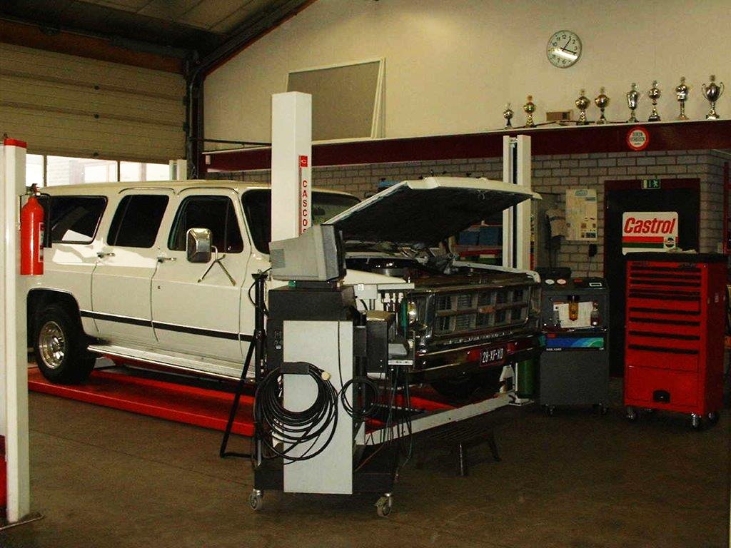Een witte Chevrolet Suburban op de brug in de werkplaats van ATC, met het diagnoseapparaat ernaast